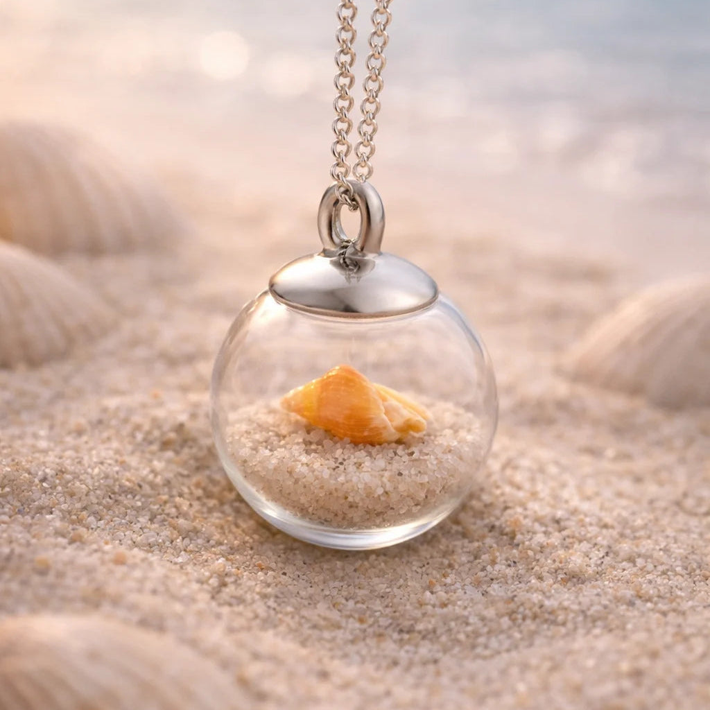 orange Muschel in Glasperle hängt an einer Edelstahlkette in Strandszene