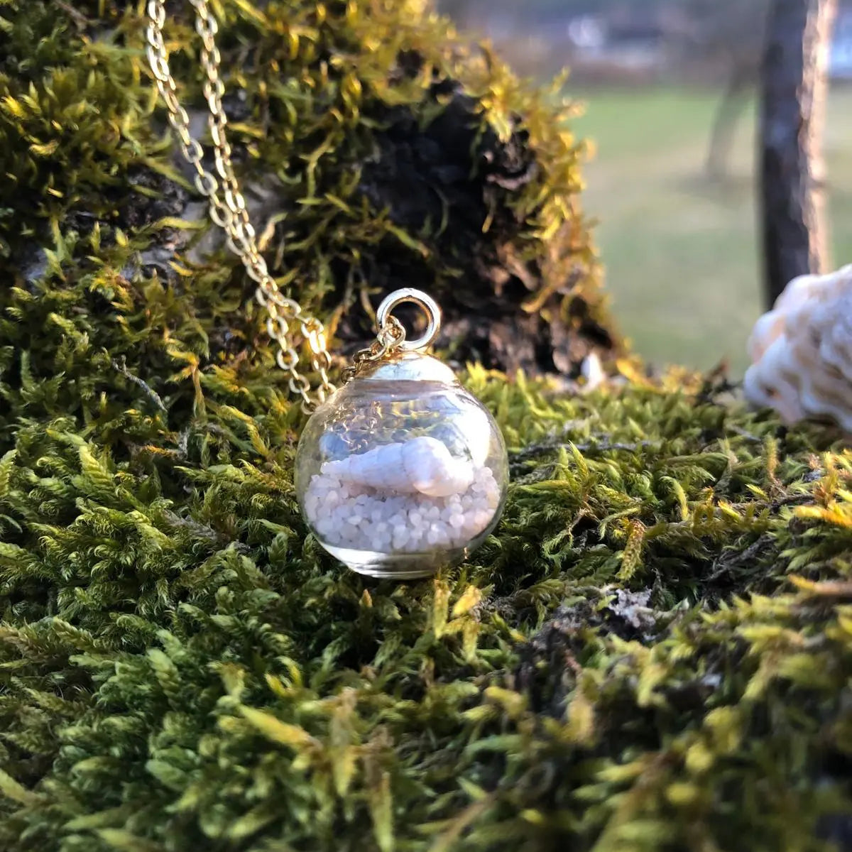 Weiße Muschel in Glaskugel hängt an einer Edelstahlkette in Strandszene