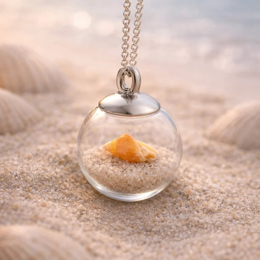 orange Muschel in Glasperle hängt an einer Edelstahlkette in Strandszene