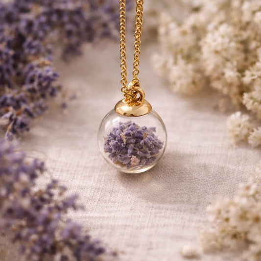 Lila Lavendelblüten in einer Glasperle mit einer goldenen Kette, umringt von getrockneten Blüten
